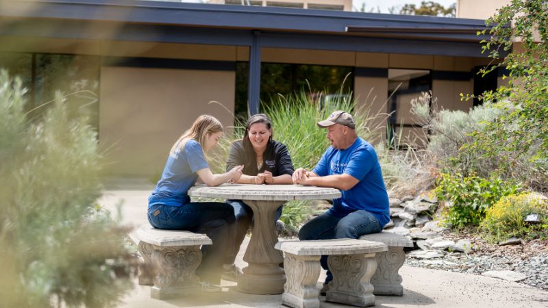 Three people sit around a stone table in the Omak campus courtyard