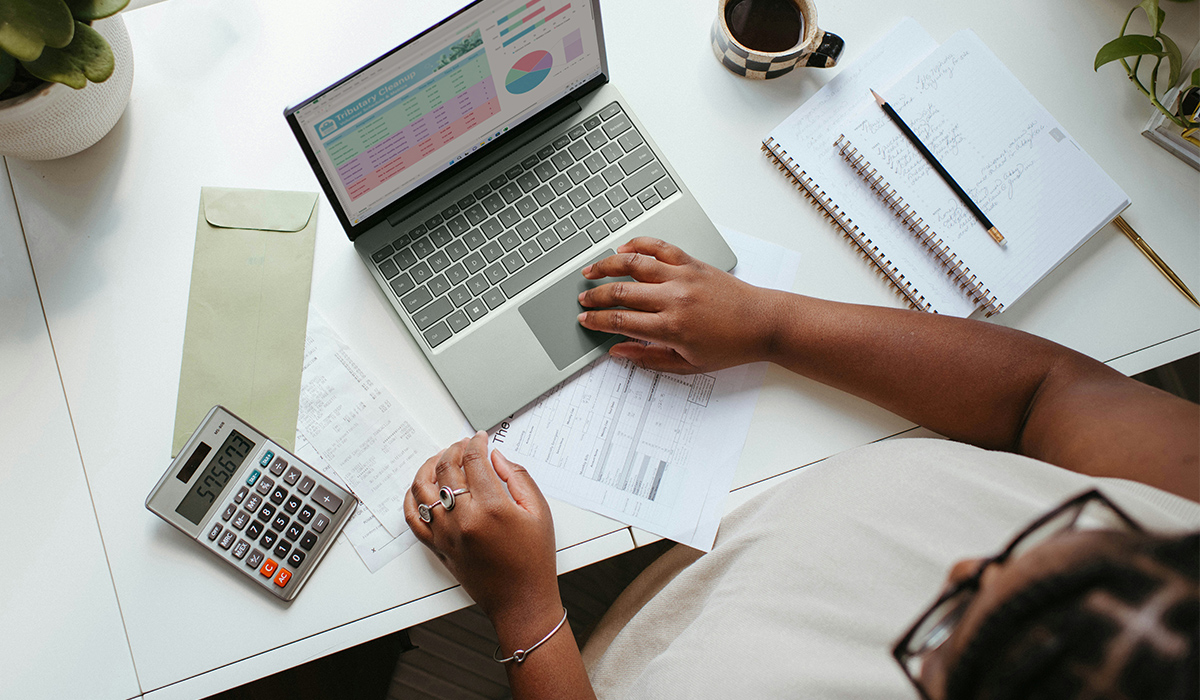 A person sits at a desk in front of a laptop with accounting information on the screen.