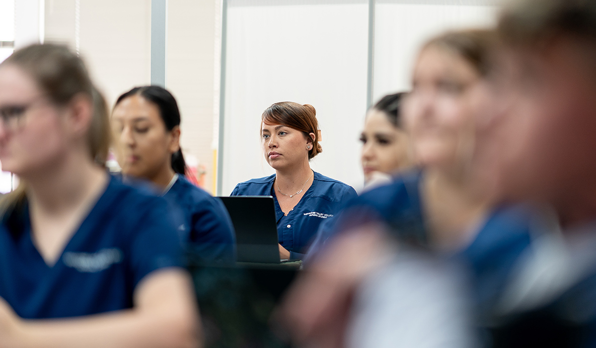 A WVC Omak nursing student wearing blue scrubs sits among other nursing students in a classroom.