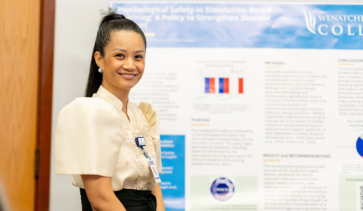 A WVC Omak LPN graduate stands in front of her poster project and smiles at the camera.