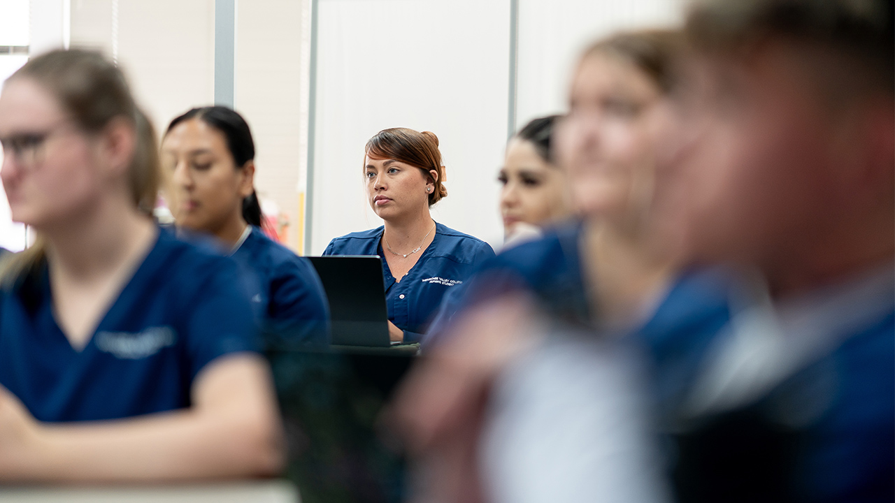WVC Omak nursing students in dark blue scrubs sit in a classroom.