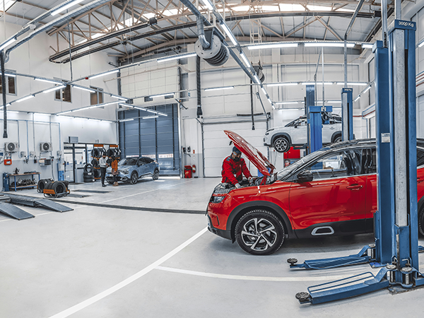 The inside of an auto repair shop, with a mechanic working on the engine of a red car.