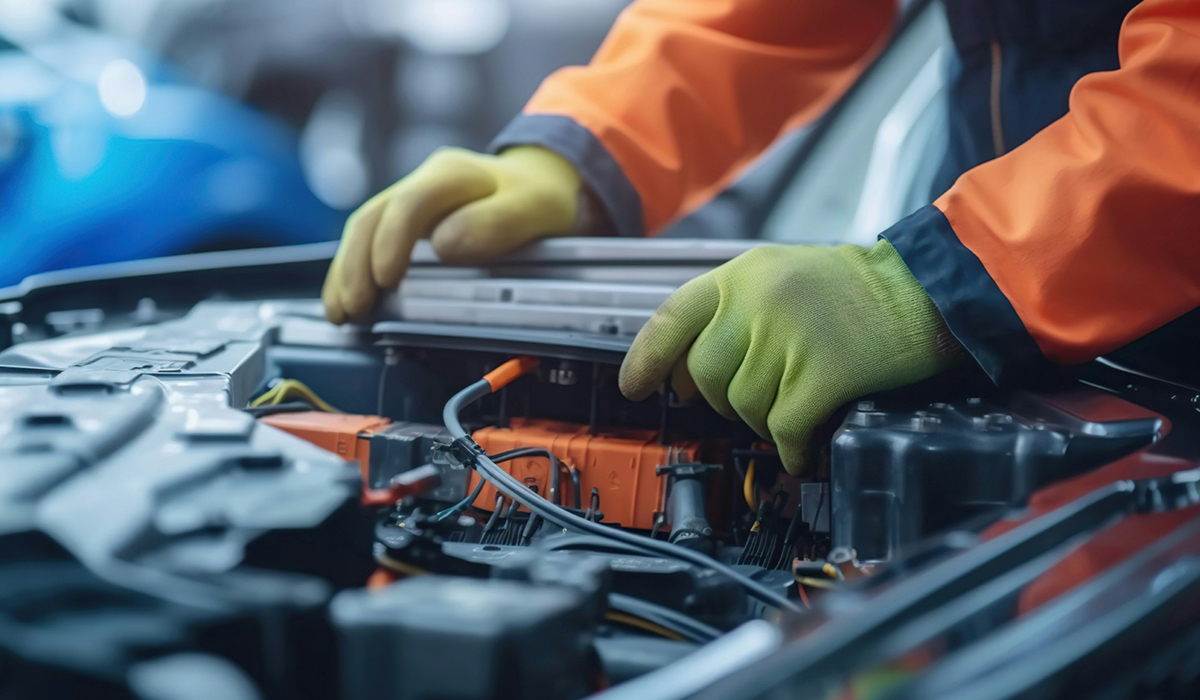 An auto mechanic wearing yellow gloves works on an electric engine.