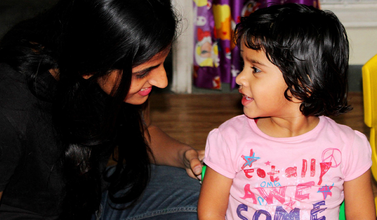 A child in a pink short smiles at a woman kneeling next to her.