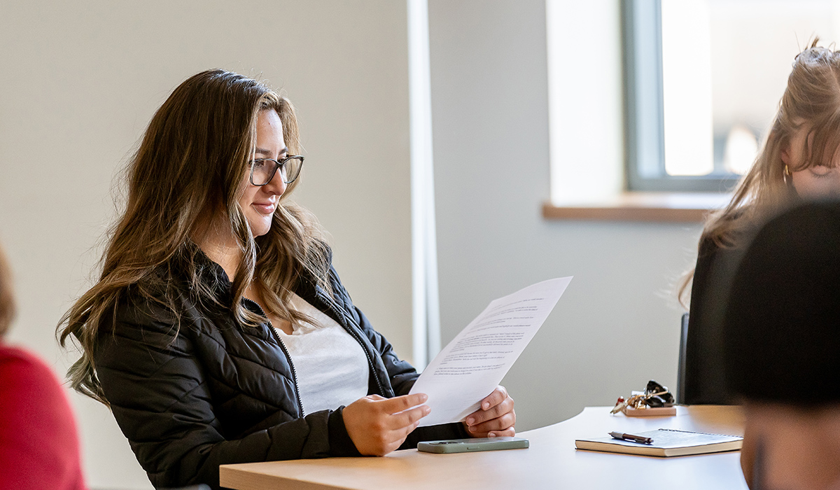 A student sits at a table and looks at a paper with typing on it.