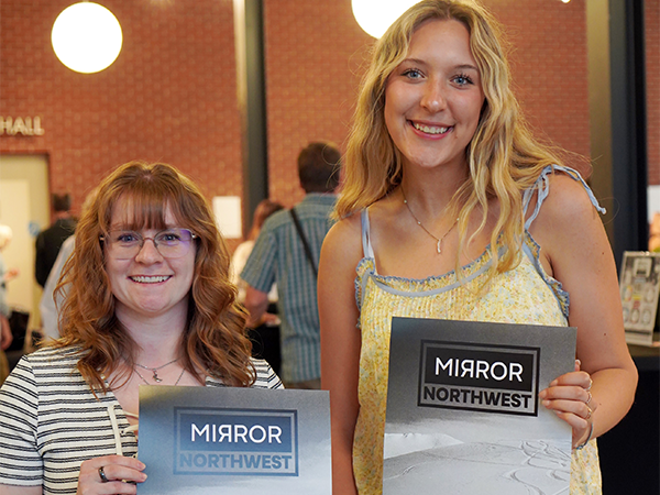 The two student editors of the Mirror Northwest literary journal hold copies of the journal's 2025 cover.