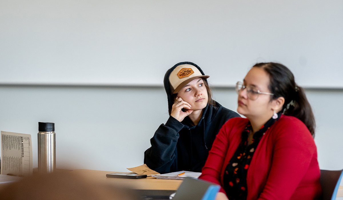 Two students sit at tables in a classroom.