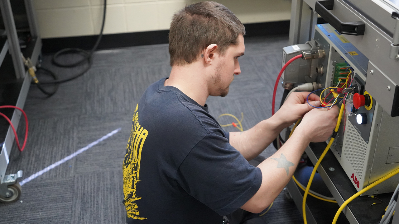 A student adjusts the wires that control a robotic arm.
