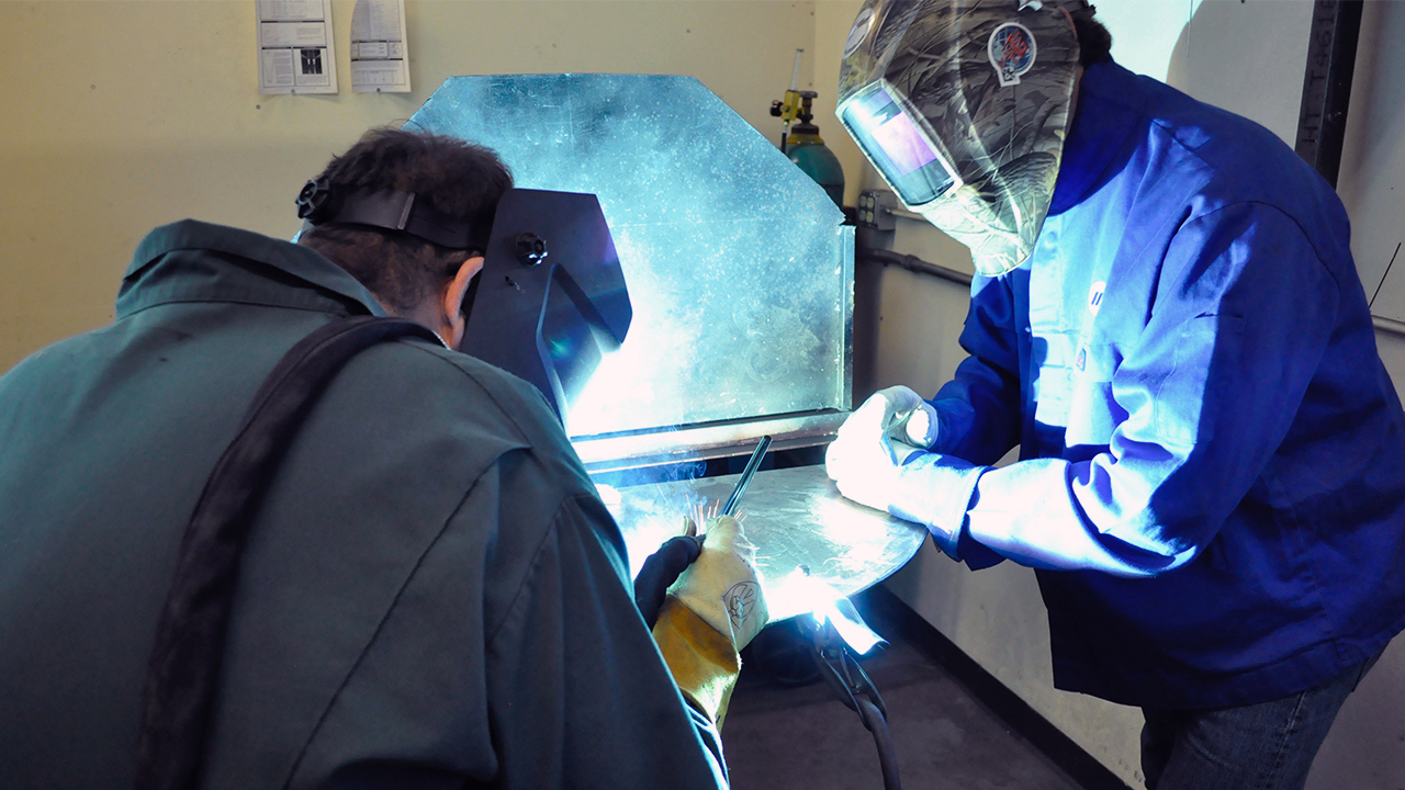 Two students wearing face shields work together on a welding project.