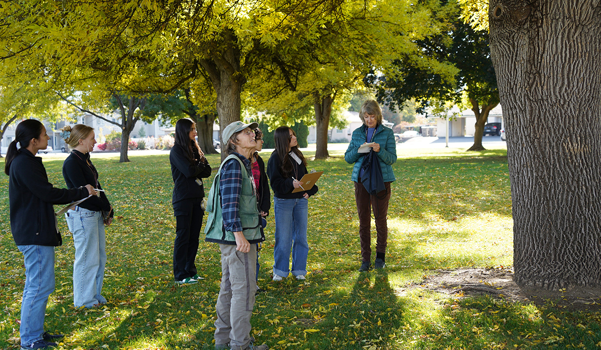 Students stand with their geography professor beneath a tree.
