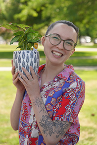 Portrait of Dr. Branwen Schaub standing outside and holding a potted plant.