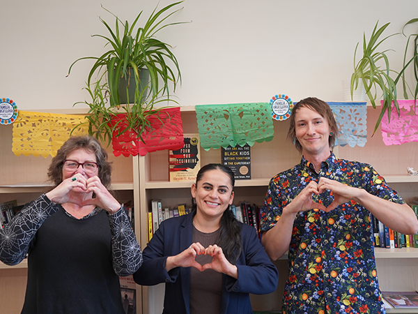 Dr. Maria I. Morales-Sanchez stands between Barbara Oldham and Saxon Spillman. They make heart shapes with their hands.