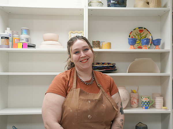 WVC Ceramics Professor Sarah Sprouse stands in front of shelves that display a variety of ceramics.