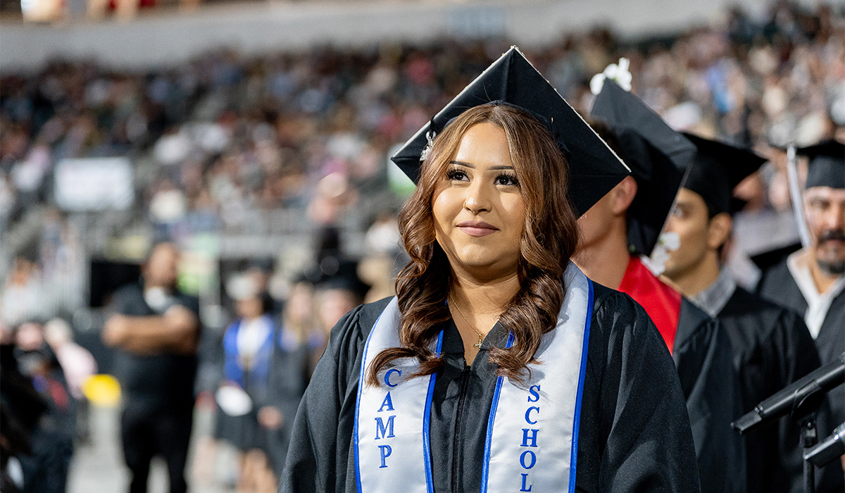 A CAMP graduate wearing graduation regalia and a CAMP Scholar stole waits her turn to go up on the stage.